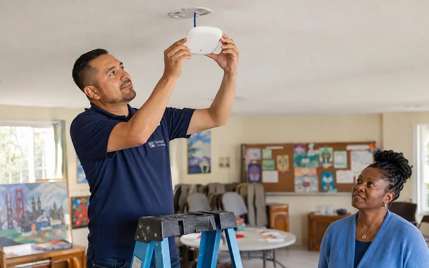 A TechInSF technician mounting a wireless access point in a community center classroom